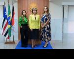 Três mulheres posando para foto. Ao fundo, banderias do Maranhão, Brasil e do TRT-16 hasteadas. 