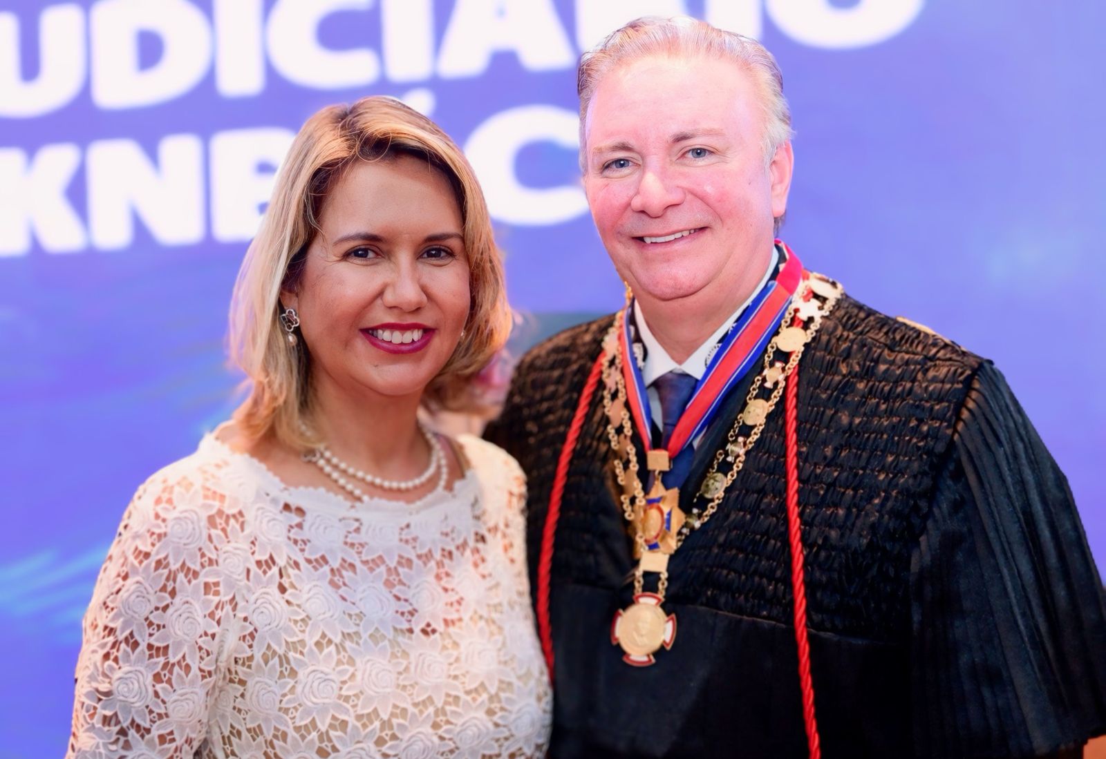 duas pessoas, uma mulher ao lado esquerdo e um homem vestido com uma toga, posam para a foto.