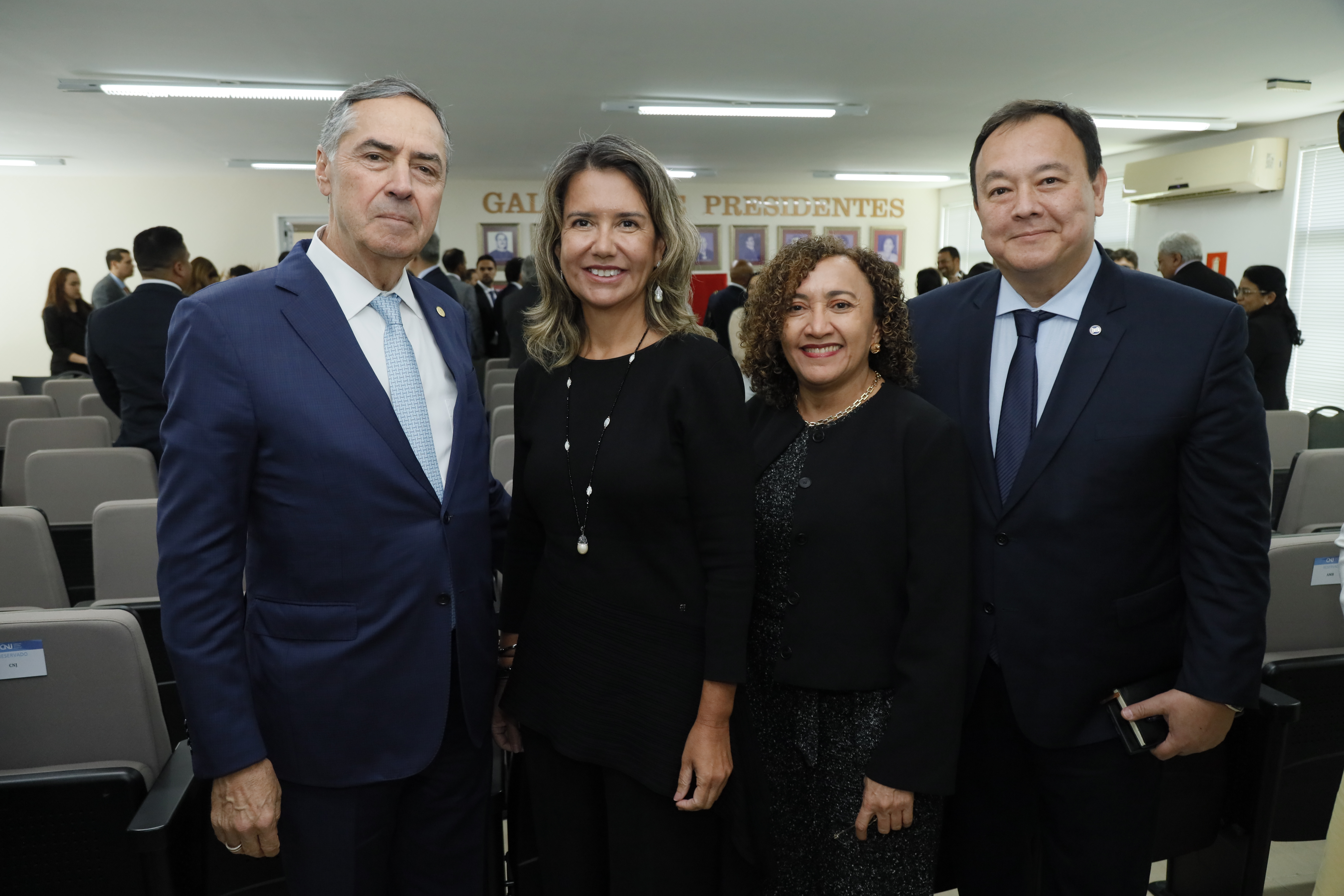 Foto mostra duas mulheres ao centro e dois homens nas extremidades. Eles estão em pé, diante de cadeiras de um auditório