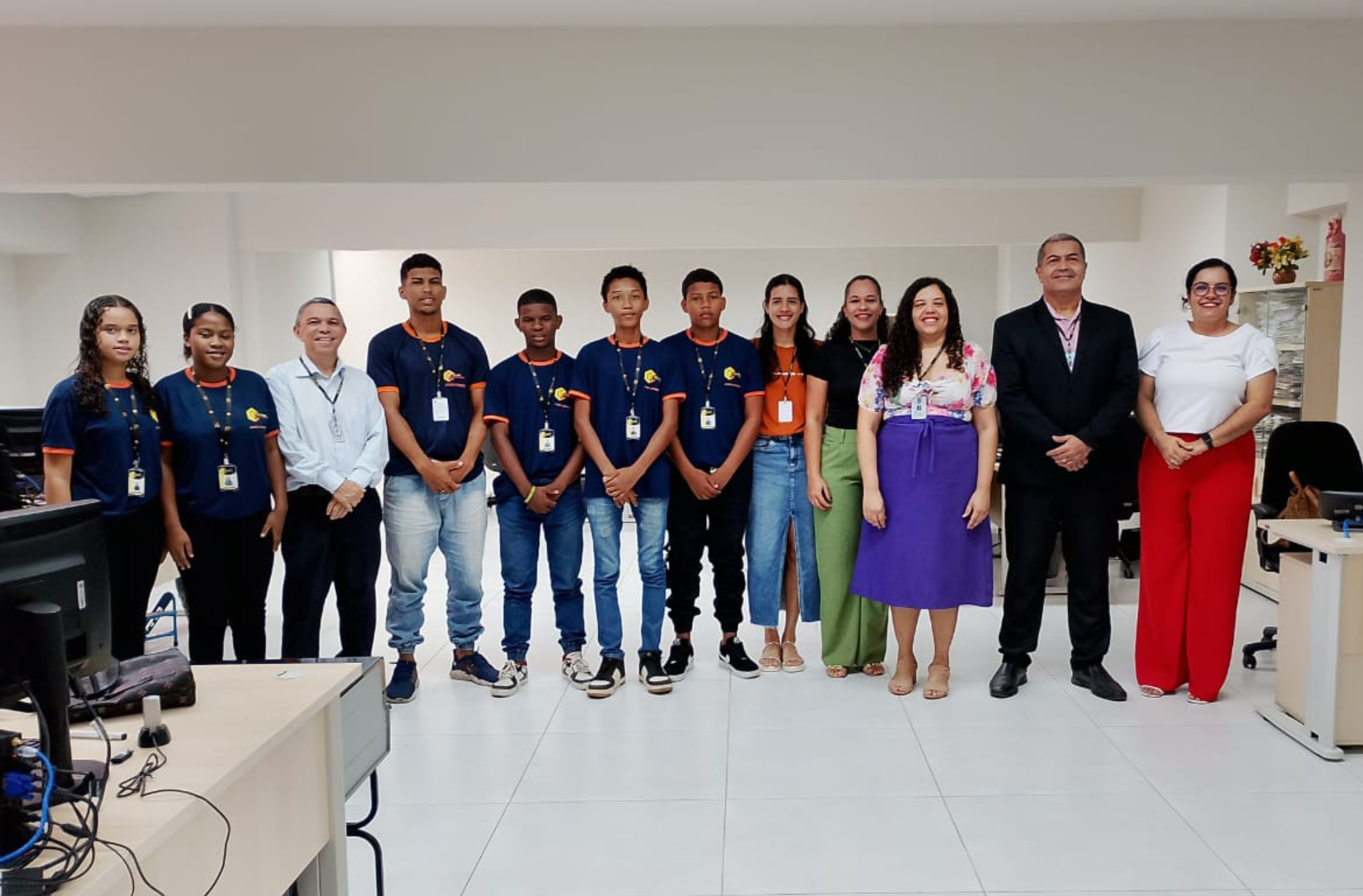 Foto de doze pessoas, entre jovens e servidores do TRT-16, de pé e sorrindo. Atrás deles, parede clara. Nas laterais, móveis de escritório em tons de bege.