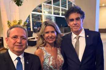 Foto mostra uma mulher posicionada ao lado de dois homens. Ambos estão com traje social.