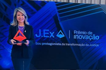 Foto mostra uma mulher segurando um troféu de acrílico. Ao lado a informação. J.Ex. Prêmio de Inovação