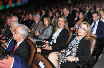 Foto mostra várias pessoas sentadas em um auditório. 