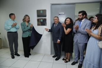 Foto mostra um grupo de pessoas em pé, ao lado de uma placa de inauguração. Uma mulher e um homem seguram um tecido azul.