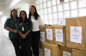 Foto mostra três mulheres em pé ao lado de caixas de papelão