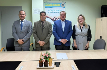 Foto mostra três homens e uma muher. Todos em pé, posicionados atrás de uma mesa de audiência