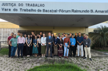 Foto mostra um grupo de pessoas posicionadas em pé na frente de um prédio. Na parte superior um letreiro: JUSTIÇA DO TRABALHO - VARA DO TRABALHO DE BACABAL