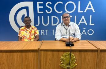 Foto mostra dois homens, sentados um ao lado do outro. Na parede do fundo, o nome Escola Judicial TRT16