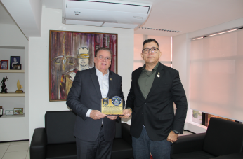 Foto mostra dois homens em pé um ao lado do outro. Ambos seguram uma placa comemorativa