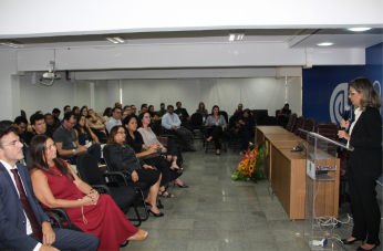 Foto mostra uma mulher em pé falando para uma platéia dentro de um auditório.