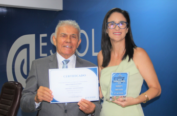 Foto mostra um homem e uma mulher, segurando um certificado e uma placa de homenagens.