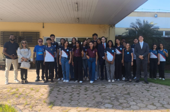 Foto mostra várias pessoas reunidas em frente a um prédio. Elas estão posicionadas um ao lado da outra.