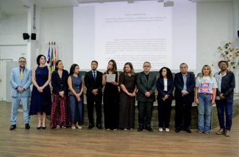 Foto mostra um grupo de pessoas em pé no centro de um auditório.