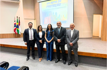 Foto mostra cinco pessoas em pé, uma ao lado da outra dentro de um auditório