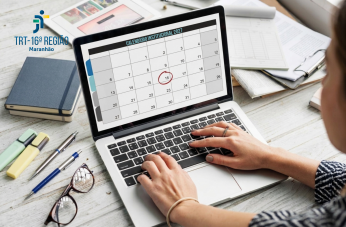 Foto de uma mesa de trabalho com mãos femininas no teclado de um notebook, em cuja tela aparece um calendário.