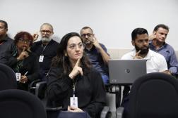 Foto mostra pessoas sentadas com as mãos na altura do rosto fazendo sinais de Libras