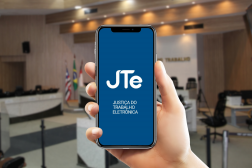 Arte feita com uma imagem de uma mão segurando um celular. Na tela, a informação: JTe Justiça do Trabalho Eletrônica