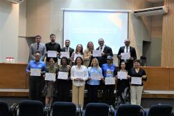 Foto mostra várias pessoas em pé, em um auditório. Todas seguram um certificado.