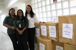 Foto mostra três mulheres em pé ao lado de caixas de papelão