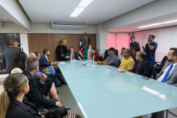 Foto mostra pessoas sentadas em volta de uma mesa de reunião