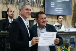 Foto mostra dois homens em pé um ao lado do outro. Eles seguam um diploma. 