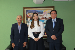 Foto mostra dois homens e uma mulher. Eles estão em pé, lado a lado. Ao fundo uma parede verde e um quadro colorido