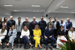 Foto mostra um grupo de pessoas no meio de um auditório. No primeiro plano algumas pessoas estão sentadas, ao fundo outra parte está em pé.
