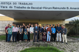 Foto mostra um grupo de pessoas posicionadas em pé na frente de um prédio. Na parte superior um letreiro: JUSTIÇA DO TRABALHO - VARA DO TRABALHO DE BACABAL
