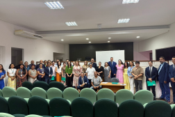 Foto mostra várias pessoas em pé, na parte de frente de um auditório.