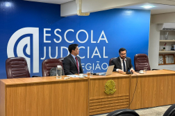 Foto mostra dois homens sentados à mesa de honra em uma auditório. Ao fundo o nome Escola Judicial
