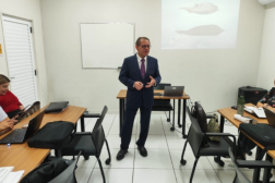 Foto mostra um homem usando um terno escuro, posicionado em pé no meio de uma sala de treinamento