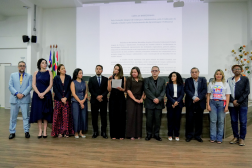 Foto mostra um grupo de pessoas em pé no centro de um auditório.