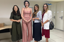 Foto mostra 4 mulheres uma ao lado da outra. Todas estão em pé e dentro de uma sala