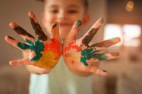 Imagem de uma criança mostrando as mãos coloridas com tintas
