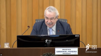 Imagem com fundo em madeira, ao centro o presidente do TST, Ministro Emmanoel Pereira, sentado em bancada do Plenário do TST, tendo a sua frente uma tela de computador, microfones, à frente da bancada placa com seu nome e cargo, e ao lado logomarca do TST