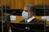 Foto do ministro Lelio Bentes Corrêa, do Tribunal Superior do Trabalho, sentado em sua bancada, em frente a um monitor, usando máscara branca, trajando toga escura, camisa branca e gravata listrada