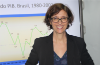 Foto da professora doutora da Unicamp Marilane Teixeira durante aula ministrada na 17ª Semana de Formação de Magistrados. Marilena tem cabelos castanhos claros curtos, está usando óculos e vestindo blazer preto sobre roupa estampada