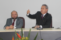 Imagem do desembargador Carvalho Neto sentado ao lado do juiz Saulo Fontes e de frente para o auditório. O desembargador veste terno terno escuro e gesticula com o braço direito. O juiz veste terno cinza.