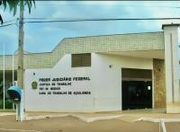 Imagem da fachada da sede da VT de Açailândia na cor branca, com porta de vidro em tom escuro, denominação da Vara Trabalhista, sendo possível visualizar o céu, um poste e um orelhão. 
