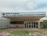 Foto da sede da Vara do Trabalho de Bacabal, antes da fachada principal há um canteiro com grama, na fachada também se vê portas de vidros de acesso à sede, além de outros canteiros na frente e plantas nas laterais, na parte superior da fachada se vê o brasão nacional e ao lado está escrito: Justiça do Trabalho - Vara do Trabalho de Bacabal - Fórum Raimundo B. Amaral Martins