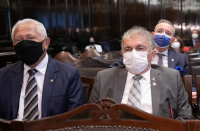 Foto dos desembargadores José Evandro de Souza (à direita, vestindo terno cinza e usando máscara branca), ouvidor judiciário do TRT do Maranhão, e Luiz Cosmo da Silva Júnior (vestindo terno azul marinho, usando máscara preta), ouvidor substituto, na abertura do IV Encontro de Ouvidores Judiciais, no Salão do Júri do Palácio de Justiça do Tribunal de Justiça de São Paulo. Na foto ainda outros participantes. Ambiente tem cadeiras de couro e armários de madeira escura).