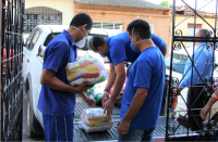 Foto de terceirizados do TRT-MA descarregando alimentos da carroceria de uma caminhonete branca no portão da Casa Acolher.