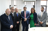 Foto no auditório da Escola Judicial durante a visita do ministro Caputo Bastos, da esquerda para a direita: juiz Saulo Fontes, desembargadores James Magno e Carvalho Neto, ministro Caputo Bastos, desembargadora Márcia Andrea e juiz Sergei Becker. Ao fundo, a parede branca, persianas cinzas e janelas de vidro