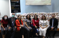 Sete pessoas sentadas no palco de auditório tendo ao fundo cestas de alimentos.