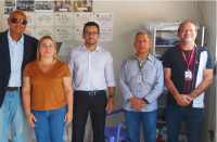 Foto de uma mulher e quatro homens em pé, à frente de parede bege decorada com fotos e diplomas