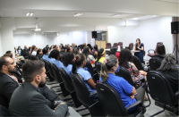 Foto de várias mulheres e vários homens sentados em cadeiras pretas participando de palestra