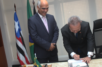 Desembargador Carvalho Neto se inclina em posição de assinatura do ato de posse, tendo ao lado o juiz Gustavo Castro.