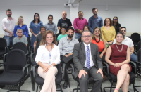 Foto de várias pessoas com parede branca ao fundo, algumas sentadas e outras em pé.