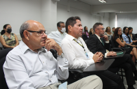 Foto de várias pessoas (homens e mulheres) sentadas em cadeiras na cor preta, no auditório da Escola Judicial