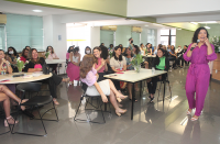 Foto de várias mulheres sentadas e de uma palestrante (que está em pé) em evento do Outubro Rosa